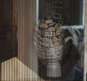 Sauna heater with pebbles and 'HUUM' branding in a wooden frame.