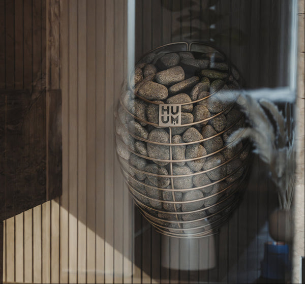 Sauna heater with pebbles and 'HUUM' branding in a wooden frame.