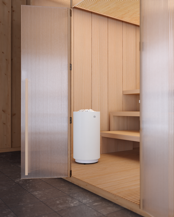 White electric sauna heater in a room with wooden walls and a glass door.