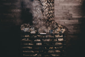 Stack of stones with a metal grate on top, emitting smoke against a wooden wall background.