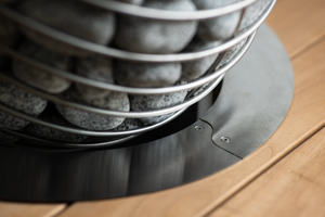 Close-up of a HUUM Drop Sauna Heater Immersion Collar with pebbles on a wooden surface