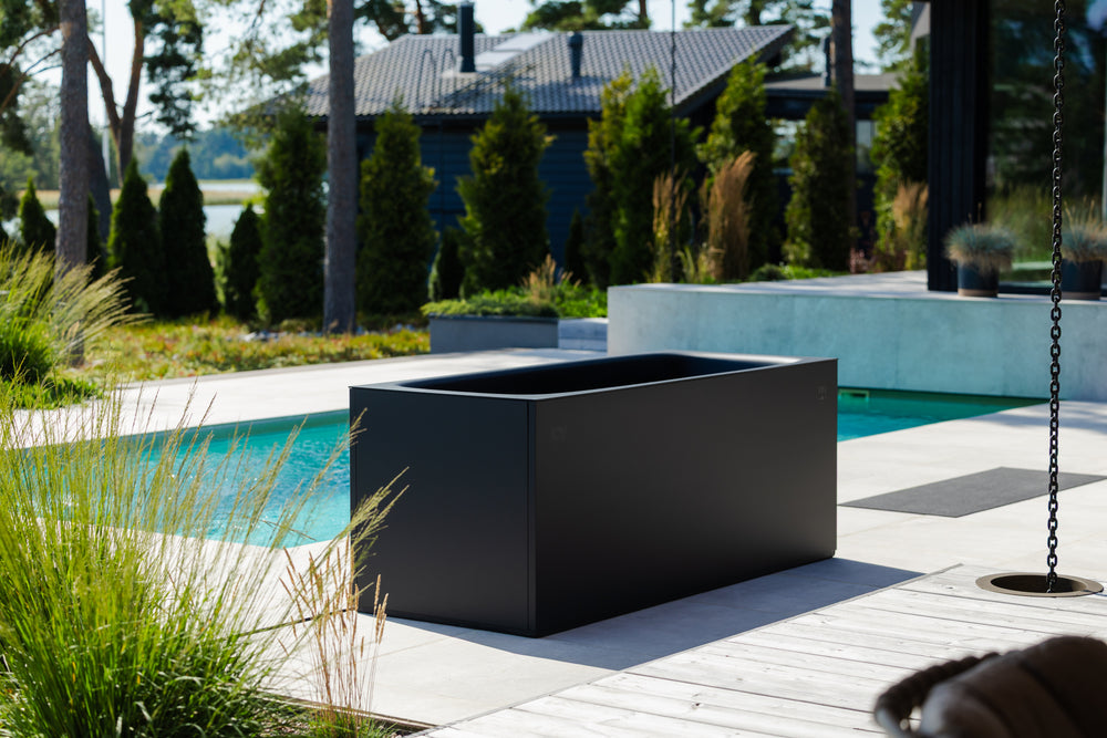Black cold plunge on a patio near a pool with a garden and house in the background