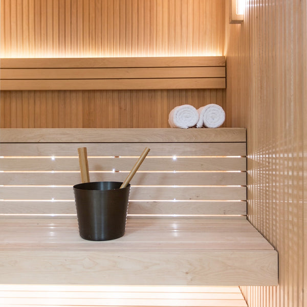 Wooden sauna interior with a black bucket and wooden sticks on a shelf.