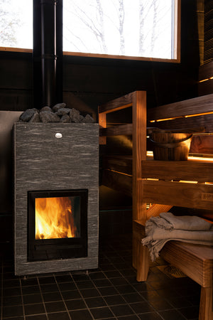 Wood-burning stove in a sauna with wooden benches and a window showing trees.