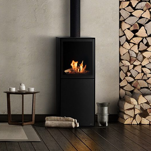 Planika Scandi free-standing ethanol fireplace from the front by a gray wall ith a cave-in for logs and chimney pipe going up. 