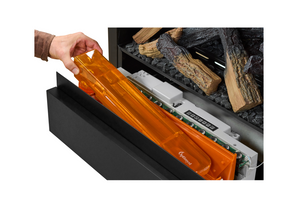 Person inserting an orange water plastic component into a electric fireplace with wood logs inside