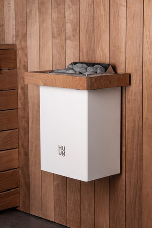 HUUM white electric sauna heater with grey stones inside in a wooden sauna