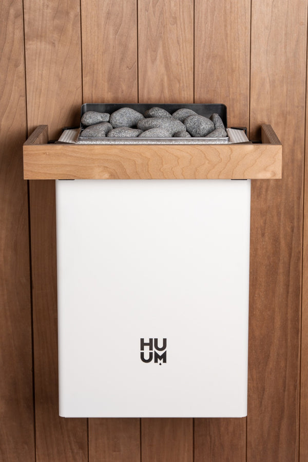 HUUM white electric sauna heater with grey stones inside in a wooden sauna