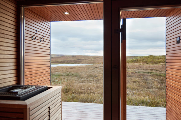 Modern cabin with wooden exterior and large windows overlooking a grassy field.