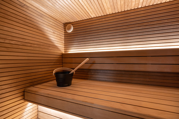 Wooden sauna interior with a black bucket and wooden spoon on a raised platform.