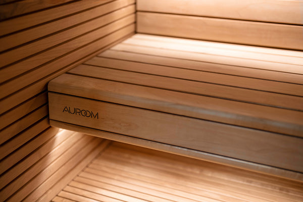 Wooden sauna bench with 'AUROM' branding in a warm, lit interior.