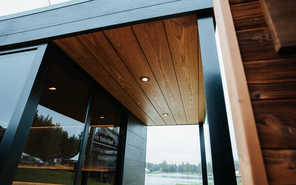 Modern architectural design with wooden and glass elements, featuring a body of water in the background.