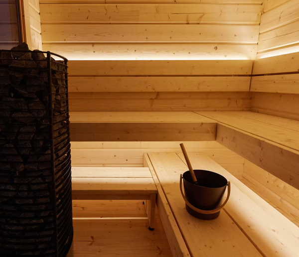 Wooden sauna interior with benches and a bucket.