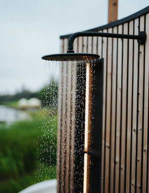 Outdoor shower head with water flowing against a wooden fence and natural background