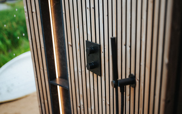 Close-up of a wooden door with metal handles and a blurred green outdoor background