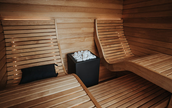Wooden sauna interior with benches and a container of stones.