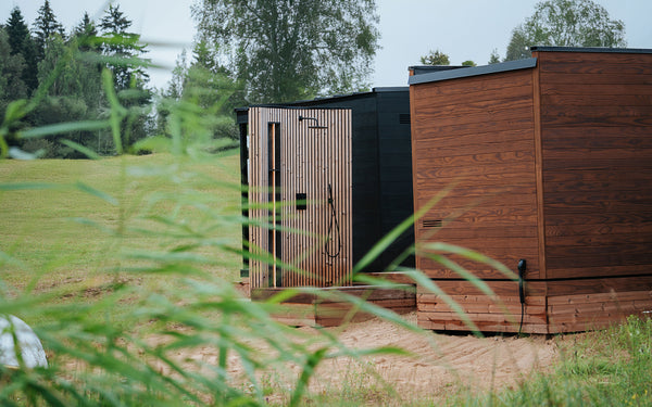 Wooden outdoor shower cabin in a natural setting with trees and grass.