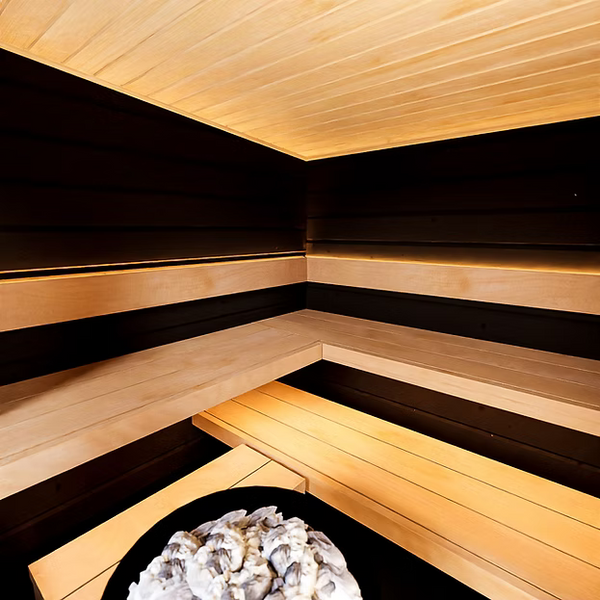 Wooden sauna with black benches and a stone heater.