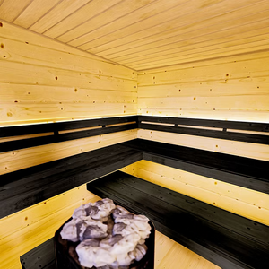 Wooden sauna with black benches and a stone heater.