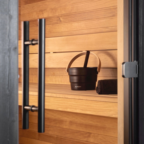 Wooden sauna with a black bucket and towel hanging on a hook