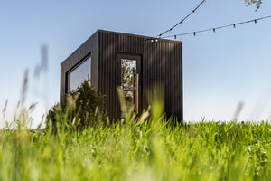 Modern blackprefab cabin in a grassy field with a clear blue sky.