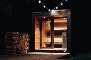 Wooden sauna with glowing interior, stacked logs, and string lights against a dark background