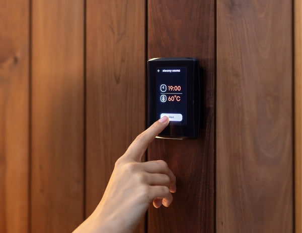 Hand pressing a digital temperature control panel on a wooden wall.