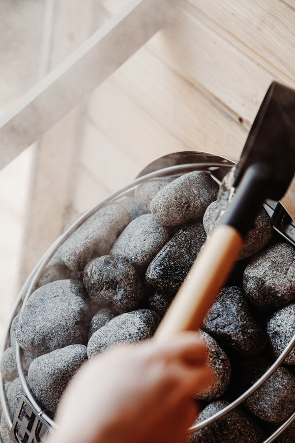 Person using a trowel to scoop stones into a circular sauna heater