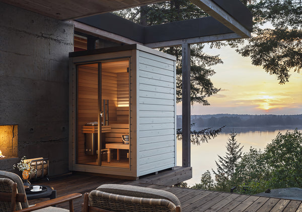 Modern outdoor sauna with a scenic view of a lake at sunset.