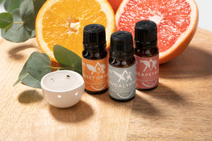 Three essential oil bottles with labels on a wooden surface with fruits and leaves.