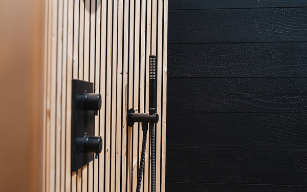 Close-up of a shower head and control panel on a black wall with wooden slats.