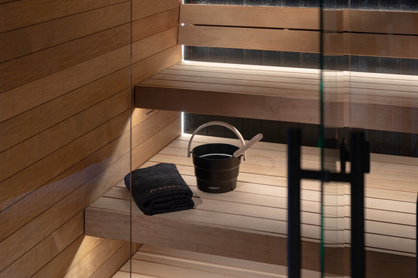 Wooden sauna interior with a bucket and towel on a bench.