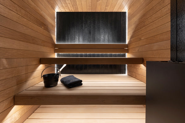 Wooden sauna interior with a black bucket and towel on a raised platform.